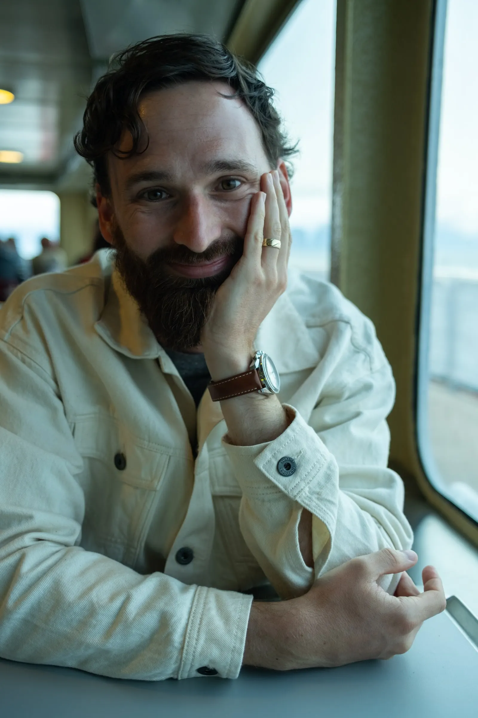 Adam, smiling, chin in hand, at a window table on a ferry.